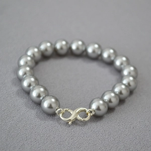 Close-up of grey high-luster pearls with silver spiral clasp on textured background