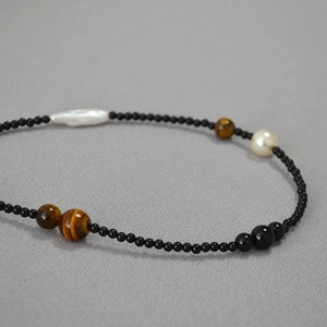Artistic beaded necklace with black onyx, tiger eye stones, and baroque pearls on grey fabric