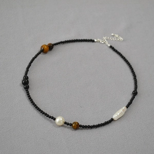 Macro detail of asymmetric beaded necklace with black agate, tiger eye, and baroque pearls