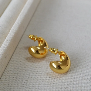 Macro shot of minimalist gold bean-shaped earrings on textured fabric background