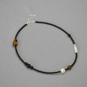Beaded necklace with black onyx, tiger eye stones and baroque pearls on grey fabric