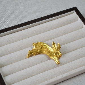 Macro shot of 3D sculpted gold rabbit brooch with handmade vintage metal texture