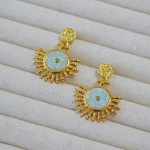 Detail of golden sunburst earrings with green gemstone and textured brass finish