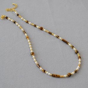 Retro beaded necklace with tiger eye stones, pearls and gold accents on grey fabric