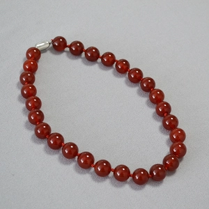 Close-up of deep red agate round beads with a silver toggle clasp on a textured background