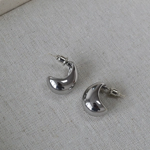 Detailed view of polished silver crescent C-shaped earrings on minimalist beige fabric