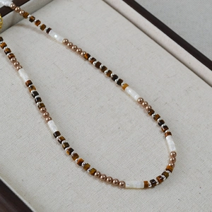 Détail macro du collier artisanal avec perles en œil de tigre et nacre naturelle