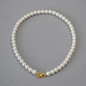 Elegant white pearl necklace with a golden infinity clasp shown on a grey background