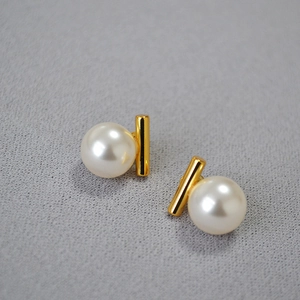 Gros plan de boucles d'oreilles en or avec perles et onyx noir sur tissu gris texturé