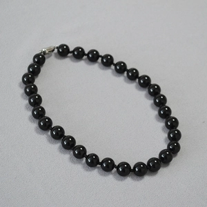 Detail of black agate beaded necklace with vintage silver yuanbao clasp on grey fabric