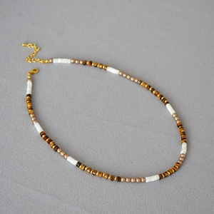 Collier bohème avec pierres œil de tigre et nacre sur fond de tissu gris texturé élégant