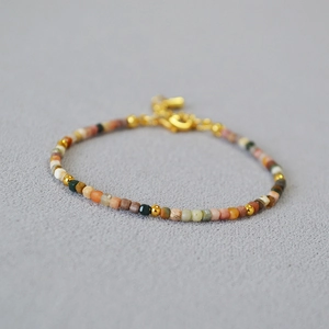 Macro shot of minimalist colorful beaded bracelet with gold spacers on textured grey fabric