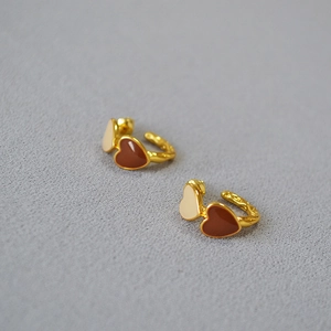 Macro shot of gold earrings with cream and brown enamel hearts on textured metal