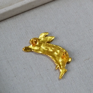 Vintage 3D sculpted golden rabbit brooch with hammered texture on beige linen background