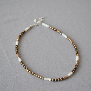 Vue macro du collier bohème avec pierres œil de tigre et nacre blanche sur tissu gris