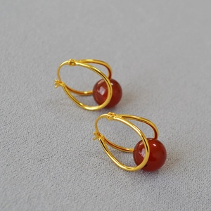 Detail view of double gold rings with red agate beads on a grey textured fabric