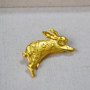 Detail of matte gold rabbit brooch with carved moon and stars on a linen background