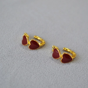 Detail of C-shaped gold hoop earrings with red enamel hearts and hammered texture