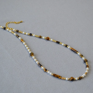 Detail of tiger eye stone and white pearl beaded necklace with gold metal accents
