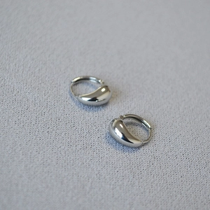Macro detail of high-polish silver drop hoop earrings on a grey textured fabric background