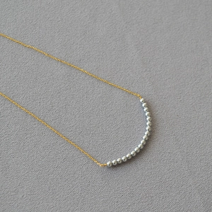 Detail of minimalist gold chain necklace featuring 16 gray pearls in curved arrangement