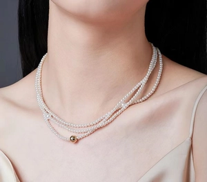 Close-up of triple-layer pearl necklace with a polished gold bead detail on a model