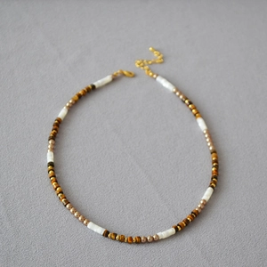 Détail du collier de perles en œil de tigre et nacre blanche sur tissu gris texturé
