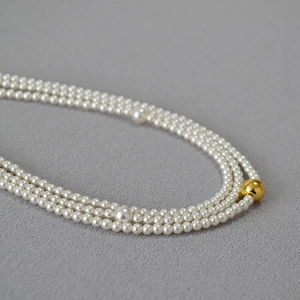Macro shot of three-layer pearl necklace with high-gloss white beads and gold accent ball