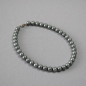 Deep grey Tahitian style pearl necklace with metallic clasp on textured surface