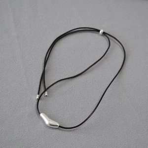 Detailed close-up of a minimalist silver organic-shaped pendant on a black cord necklace