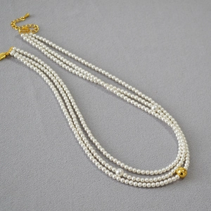Close-up of triple-layer faux pearl necklace with gold beads and adjustable clasp