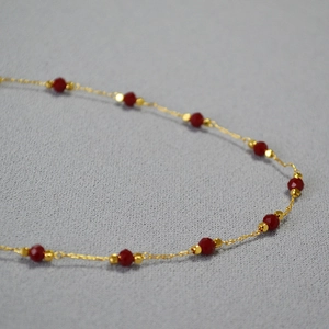 Macro shot of gold brass necklace featuring faceted cinnabar red spinel beads on a fine chain