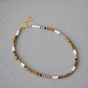 Détail macro du collier bohème en perles d'œil de tigre et nacre blanche élégante