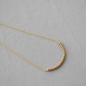 Detail of matte gold beads forming a smile curve on a minimalist necklace chain