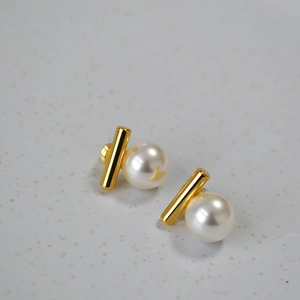 Détail des boucles d'oreilles minimalistes avec barre dorée et perle blanche ronde