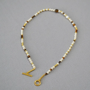 Tiger eye and pearl beaded necklace with gold toggle clasp on a textured background
