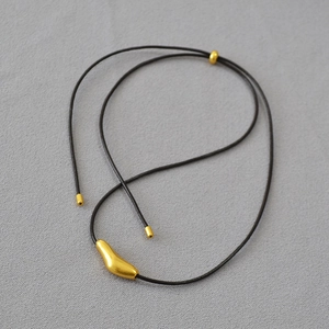 Detail of artistic gold fluid bird pendant on black leather cord over grey fabric