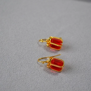 Detail view of red crystal gift box earrings with golden bow accents on a textured background