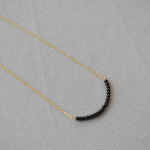 Detail of minimalist gold chain necklace with delicate black agate beads on knit fabric