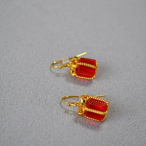 Close-up of red crystal gift box earrings with golden bow detail on grey texture