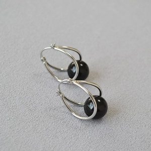 Detail of silver double hoop earrings featuring a polished black spherical bead pendant