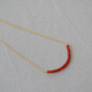 Minimalist gold necklace with a curved row of red agate beads and a delicate chain