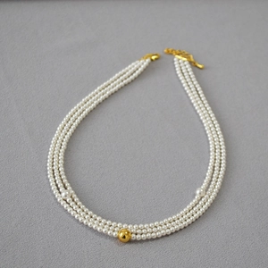 Detailed view of triple-layered pearl necklace featuring a gold mirror ball and lobster clasp