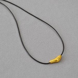 Macro detail of abstract bird gold pendant with adjustable black cord on textured surface