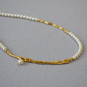 Collier rétro français avec branche dorée et perles sur fond texturé gris élégant