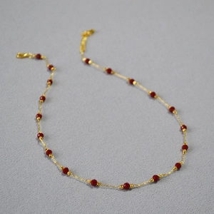 Macro detail of gold-plated brass chain with red faceted beads and lobster clasp