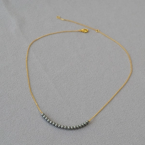 Macro detail of gold necklace with grey pearls arranged in a subtle smile arc design