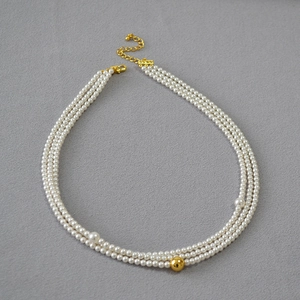 Detailed view of triple-strand pearl necklace with central gold bead on grey fabric