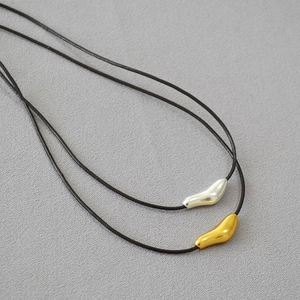 Close-up of gold and silver organic bean pendants on black leather cords for women