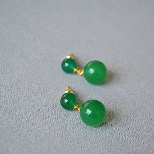 Detail of green agate double sphere earrings with gold frame on grey textured background